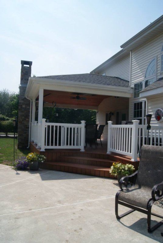 Outdoor deck with white railing, steps, and a covered section attached to a light-colored house.