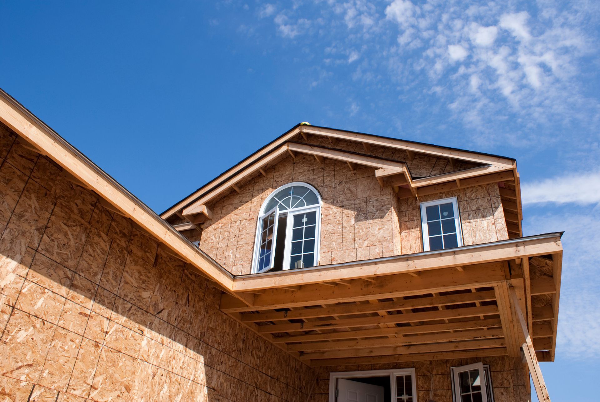 House under construction with exposed wood frame against a blue sky.