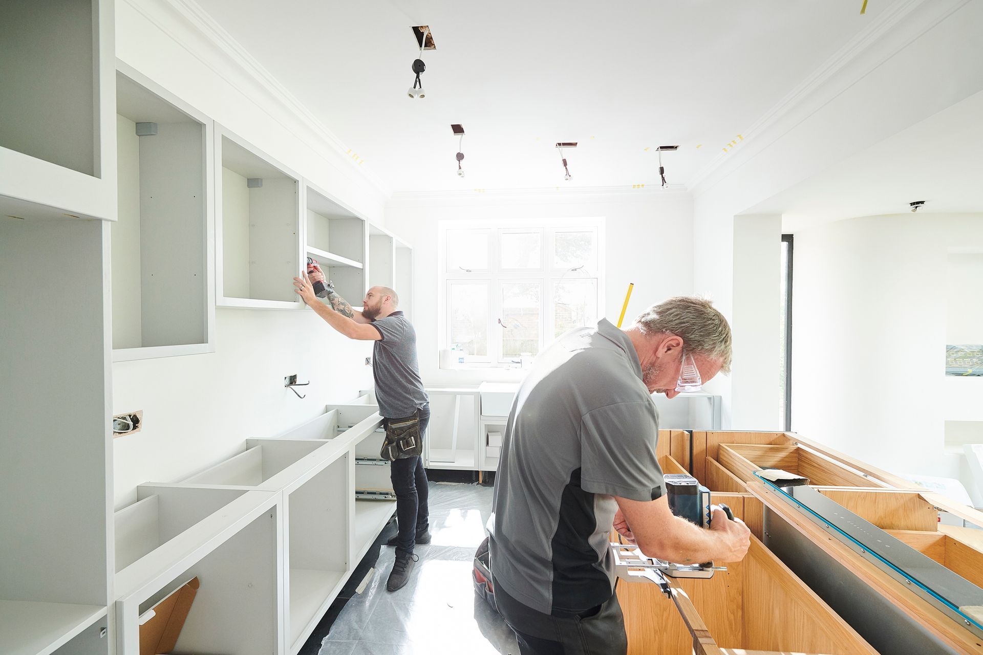 Two remodelers are working on an all-white kitchen.