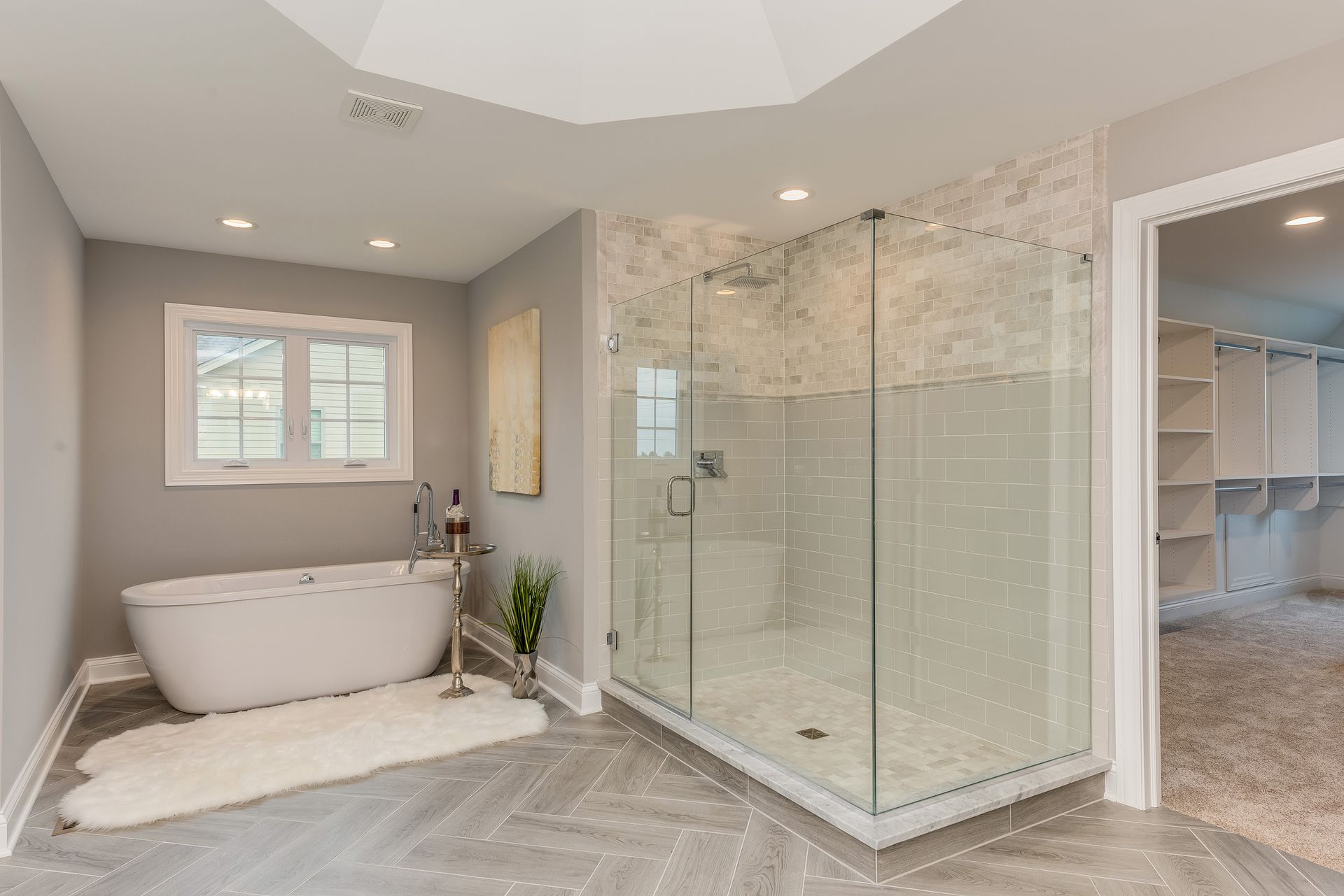 Spacious bathroom with a glass shower, soaking tub, and walk-in closet in a light, neutral color palette.