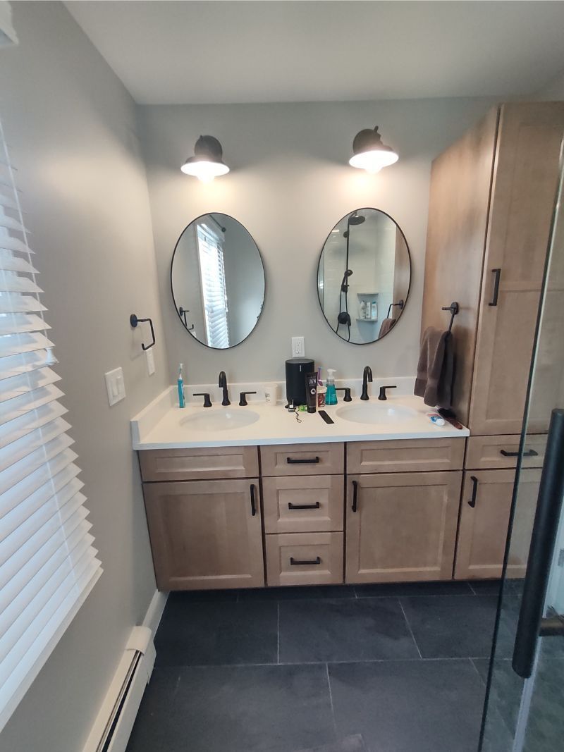 Double vanity bathroom with round mirrors, black fixtures, and light wooden cabinets.