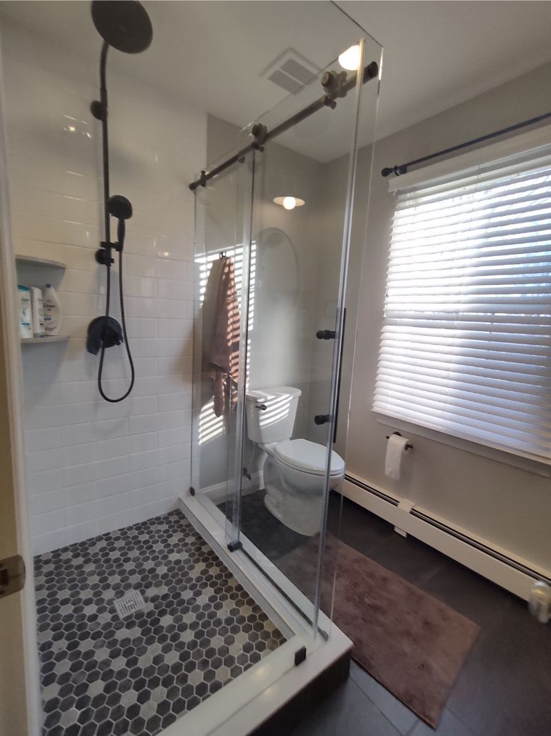 Modern bathroom with glass shower enclosure, black fixtures, and patterned floor tile.