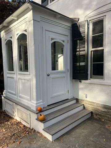 White enclosed porch with steps, door, and windows. Two pumpkins sit on the steps.