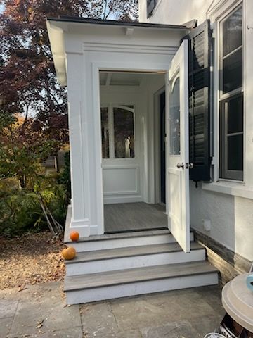 White front porch with open door, steps, and pumpkins on the ground.