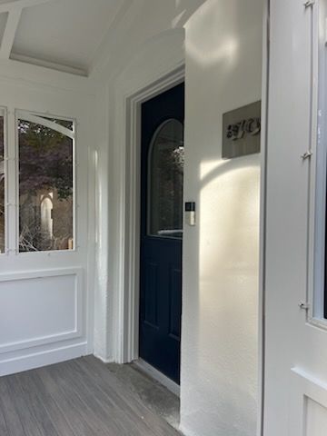 Blue front door with arched window, ring doorbell, and silver house numbers on a white porch.