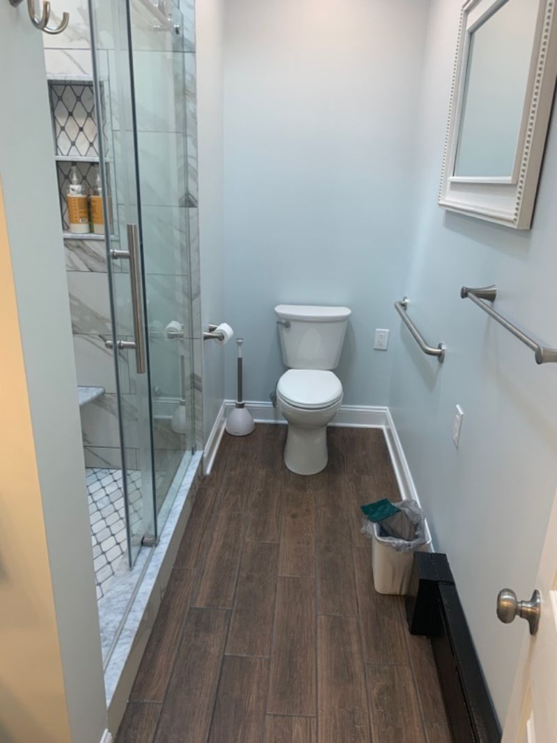 Bathroom with a shower, toilet, and wooden-look floor. Includes grab bars and a mirror.