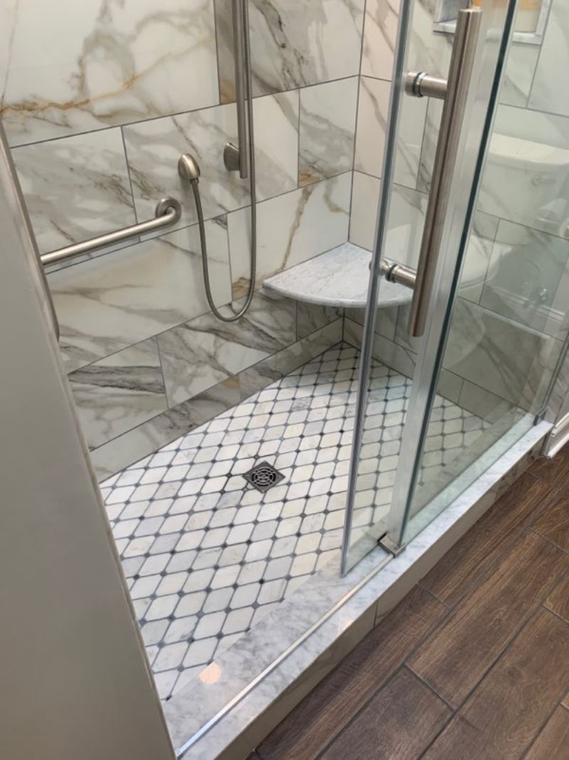 Marble tiled shower with glass door and grab bar.