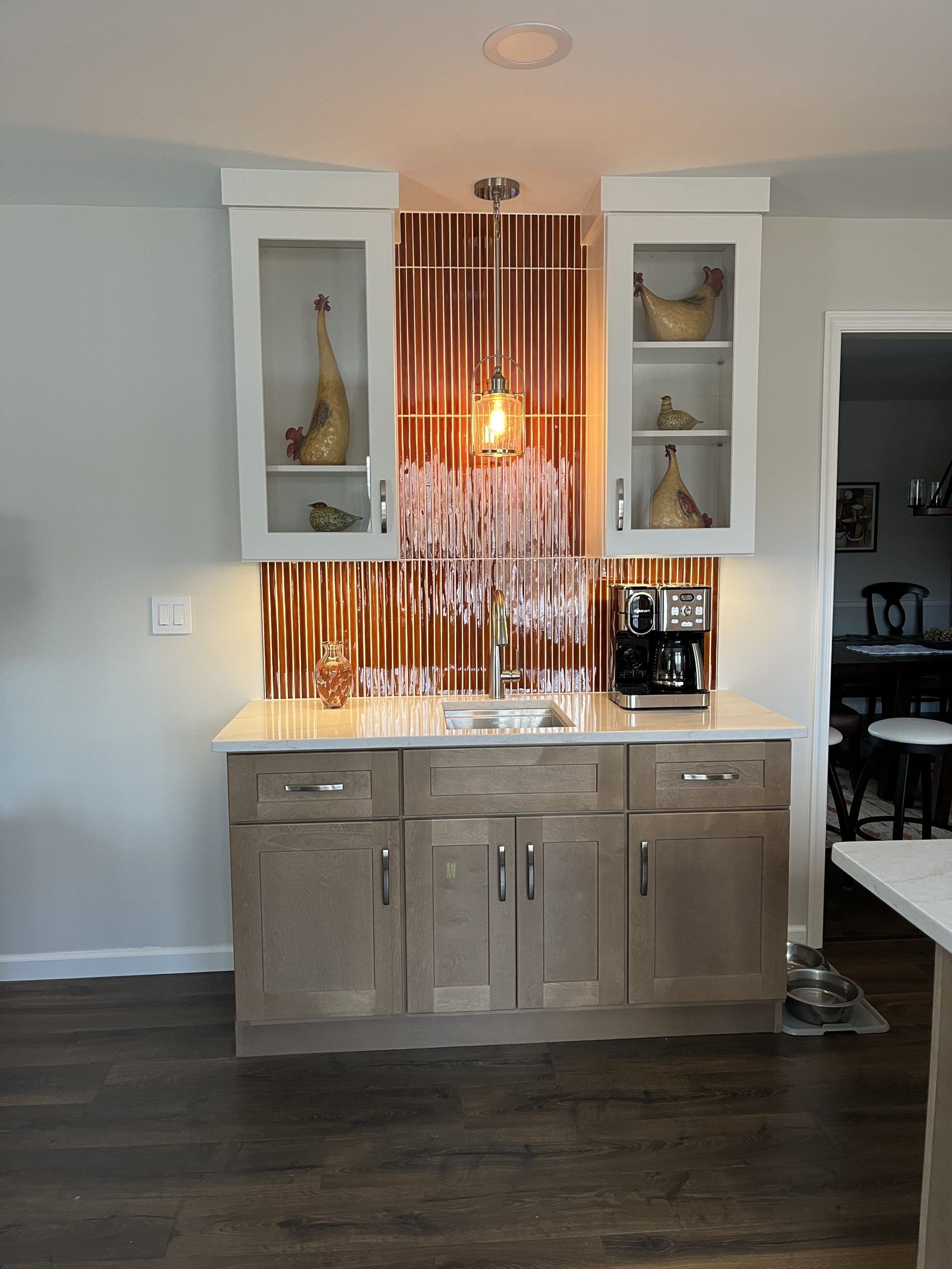 Kitchen bar with light cabinets, marble countertop, copper backsplash, and hanging crystal light fixture.