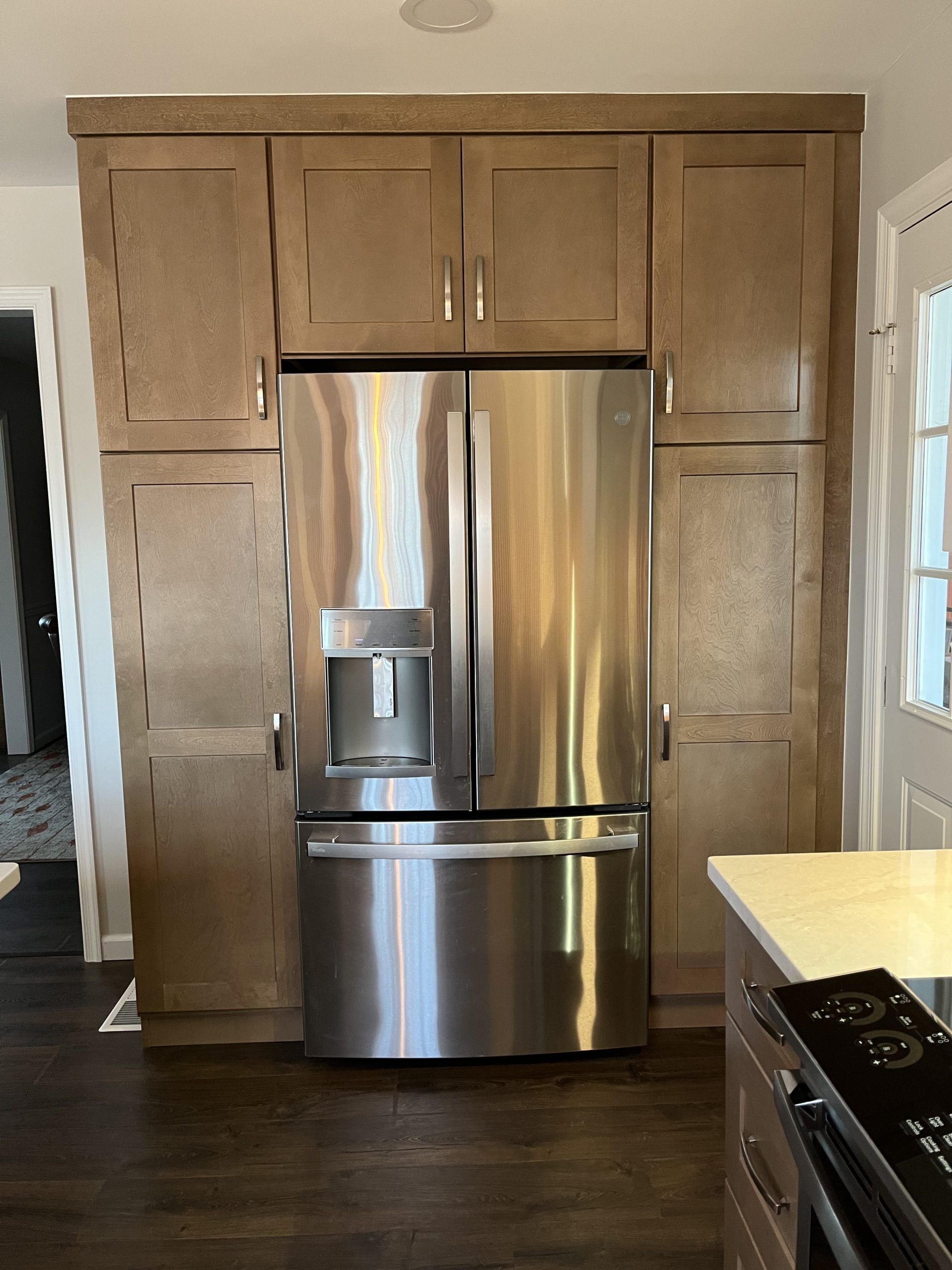 Stainless steel refrigerator built into light brown kitchen cabinets.