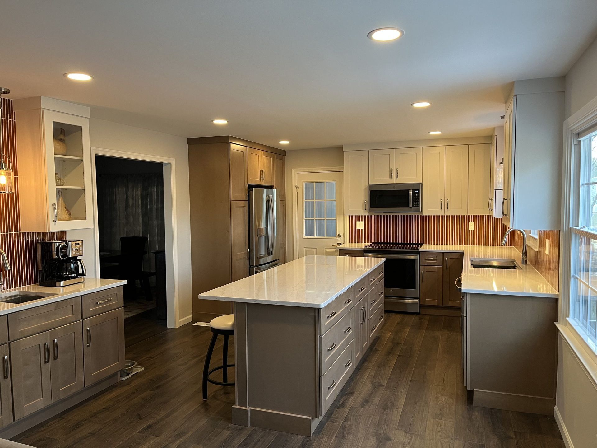 Modern kitchen with island, stainless steel appliances, neutral cabinets, and wood-look flooring.