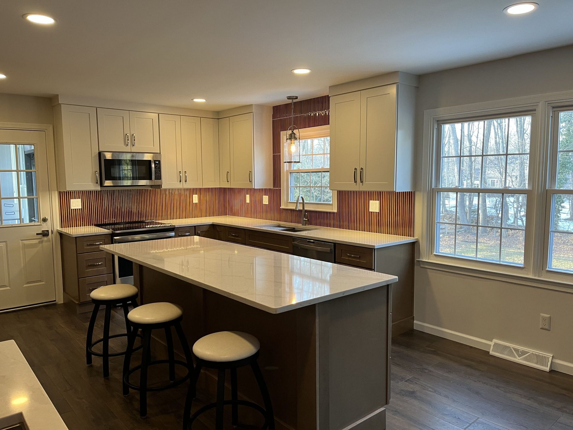 Modern kitchen with island, gray cabinets, wood and white countertops, and stools.