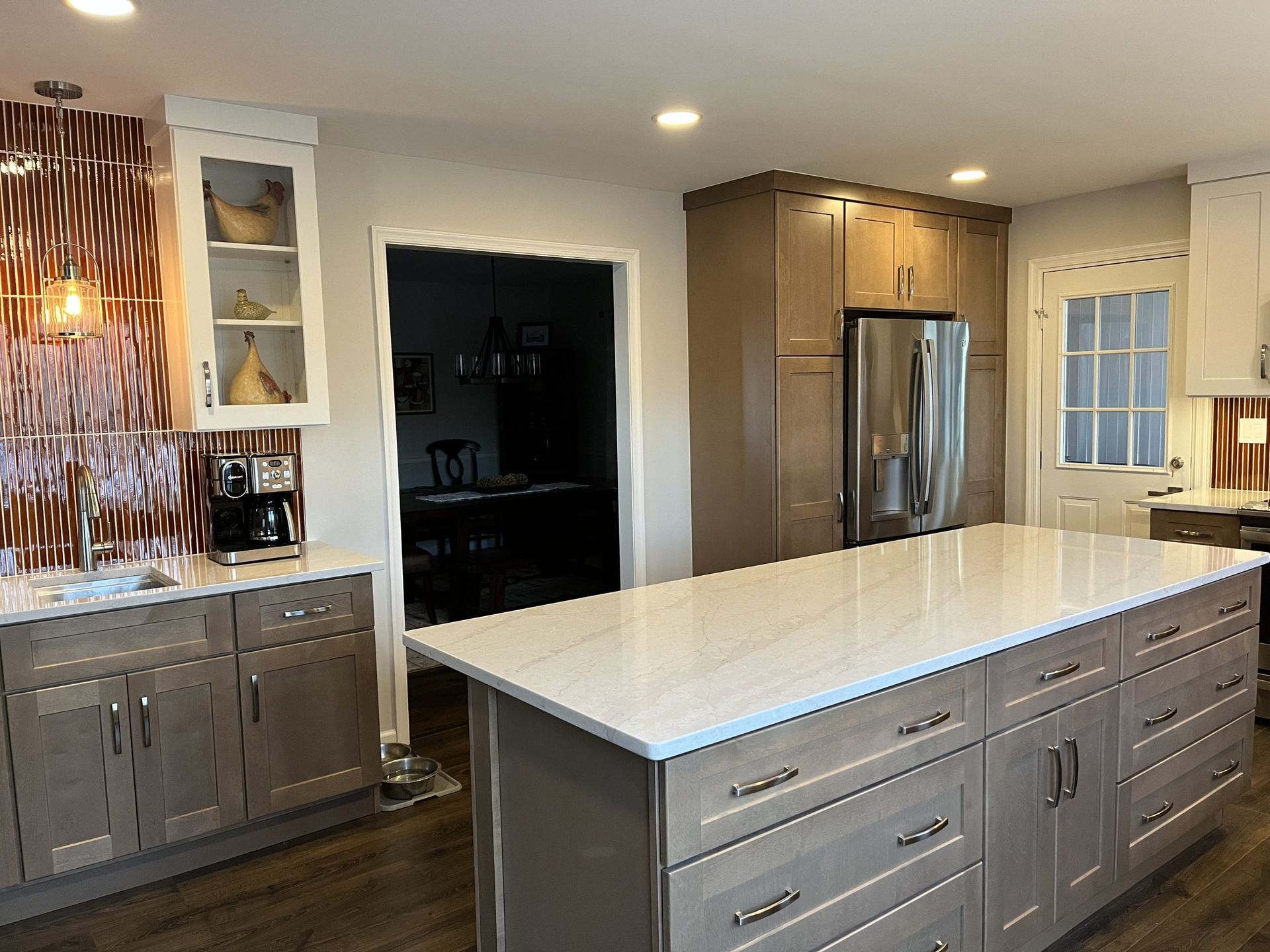Kitchen with a gray island, cabinets, and white countertop. A decorative backsplash and stainless steel appliances are also present.