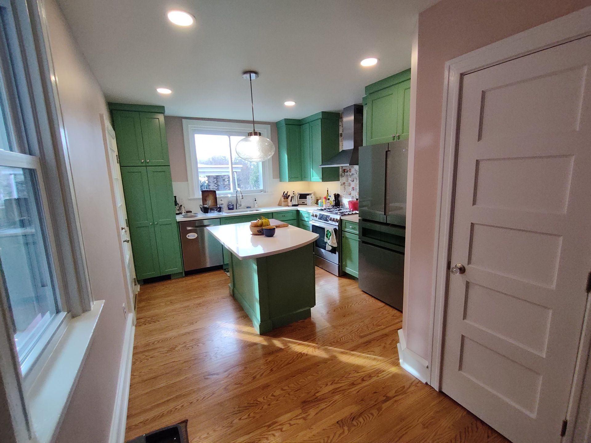 Kitchen with green cabinets and island, wood floor, and white walls.