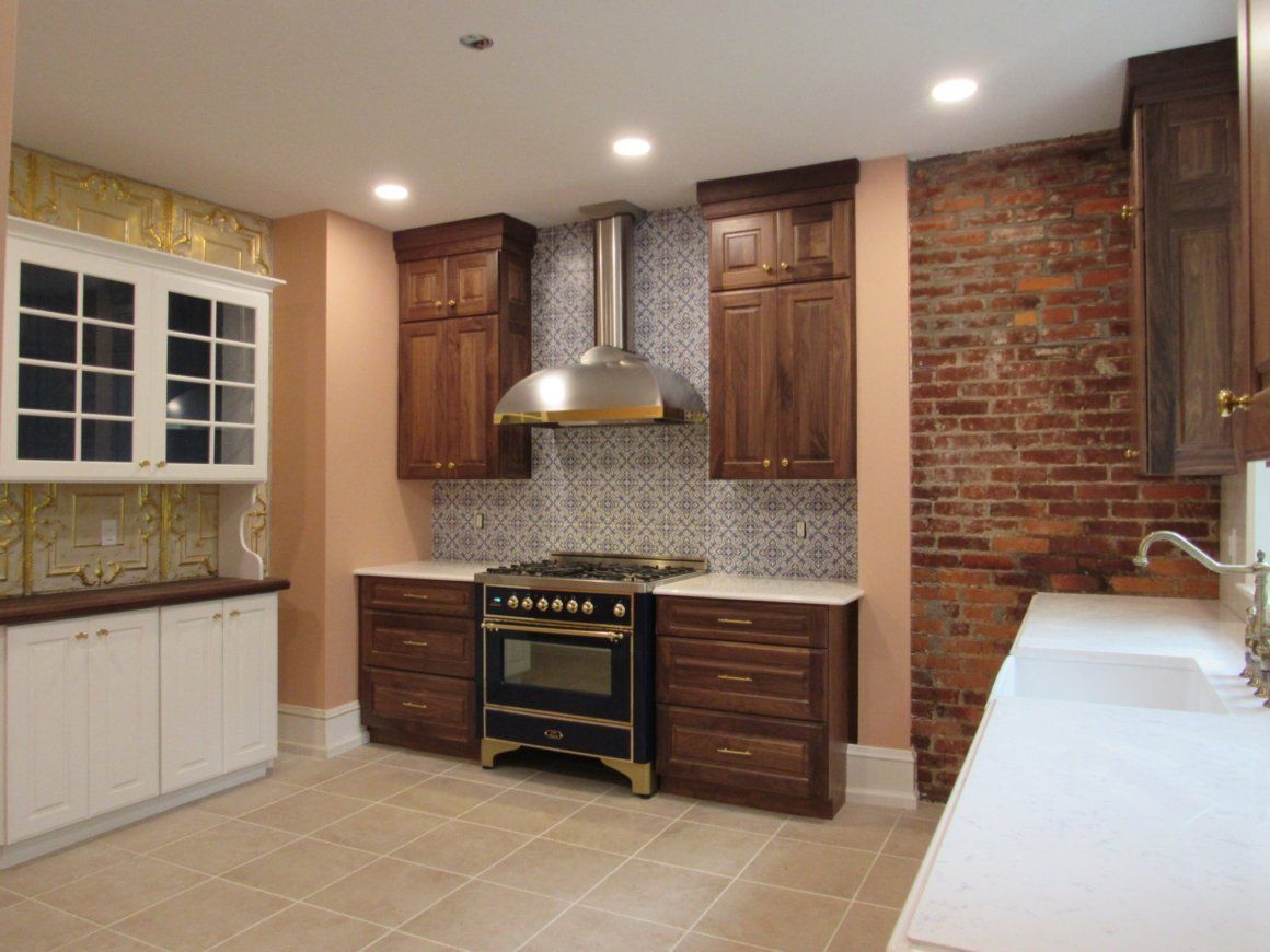 Kitchen with brick wall and dark brown cabinets, light countertops, and stove with a stainless steel range hood.