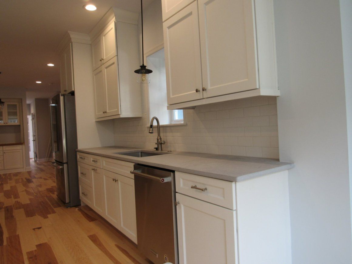 White kitchen cabinets and countertops with stainless steel appliances, and wooden floors.