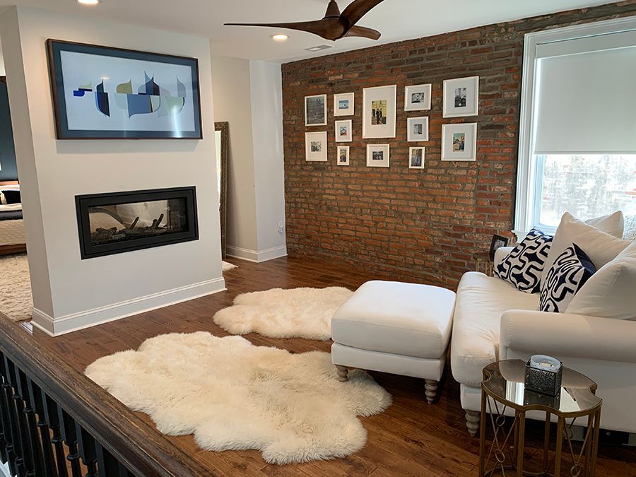 Living room with exposed brick wall, white sofa, sheepskin rugs, art, and a fireplace.