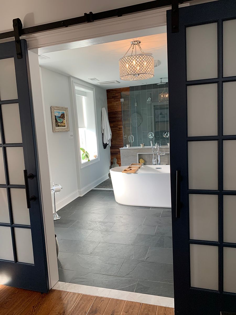Sliding blue door opens to a bathroom with a person in a white tub, chandelier, and a large window.