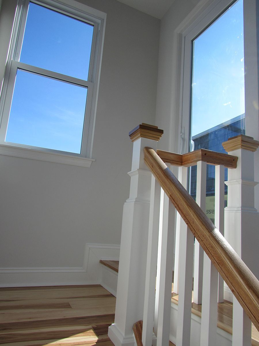 Staircase with white balusters, wooden handrail, and windows with blue sky.