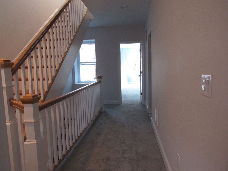 Hallway with stairs and doorway. White railing with wood trim, gray carpet, light gray walls.