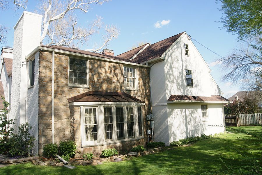Side view of a two-story house with a stone and white exterior, a curved window, and a green lawn.