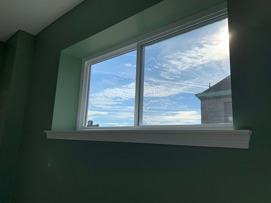 Window with white frame, white trim, and green walls. The window shows a cloudy blue sky.