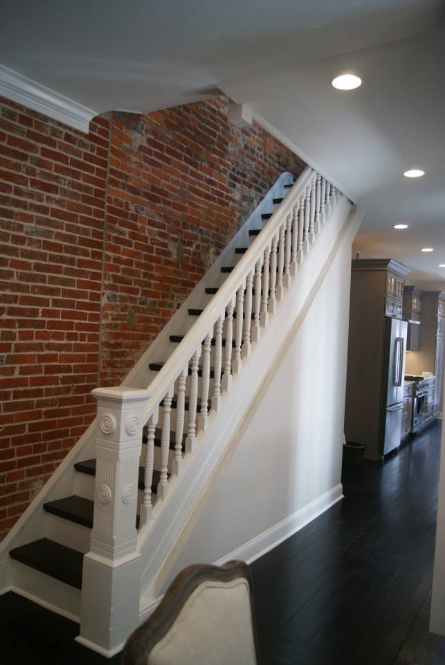 Staircase with white railing, black steps, and exposed brick wall.