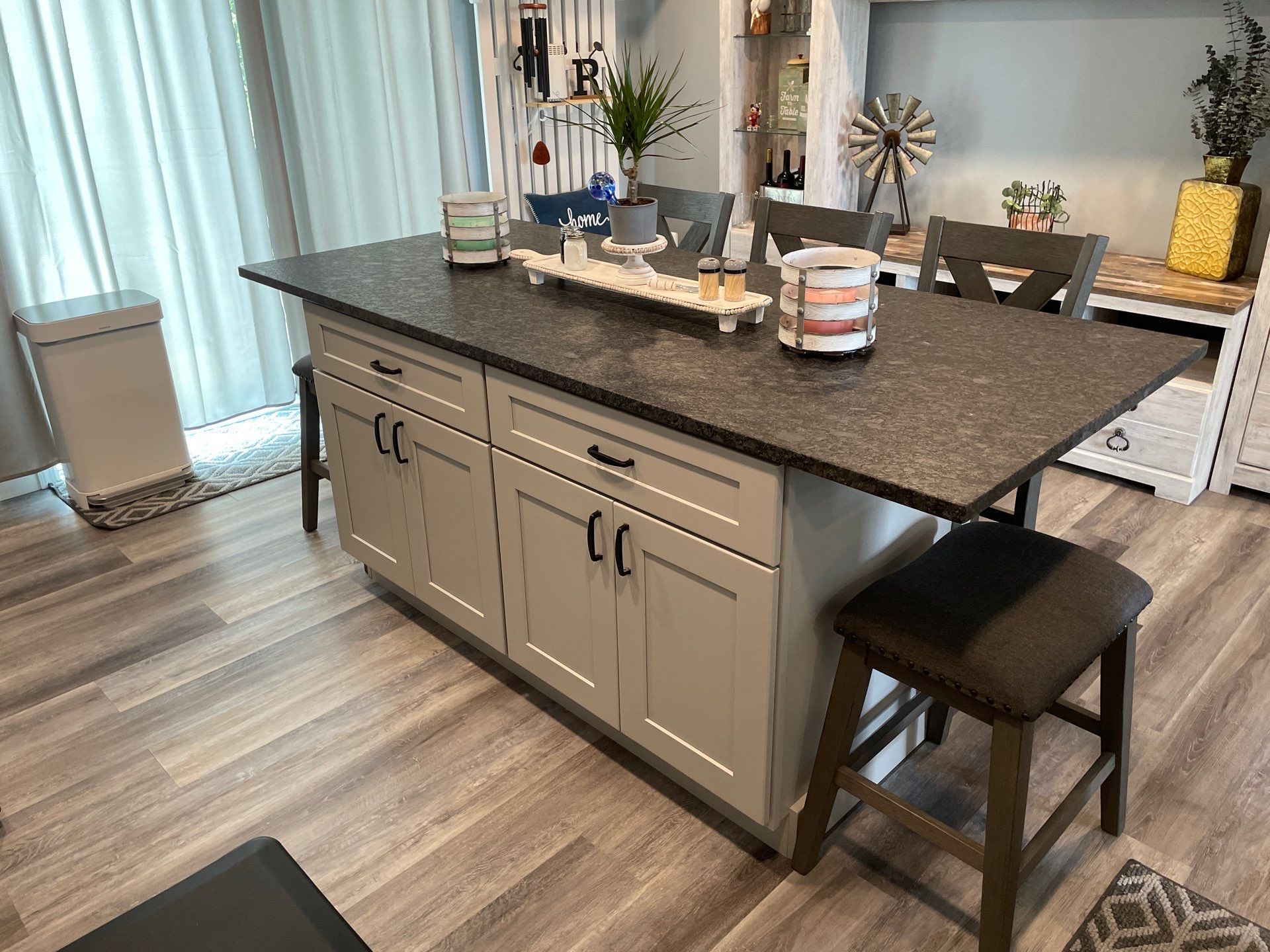 Kitchen island with gray cabinets, dark countertop, and stools.