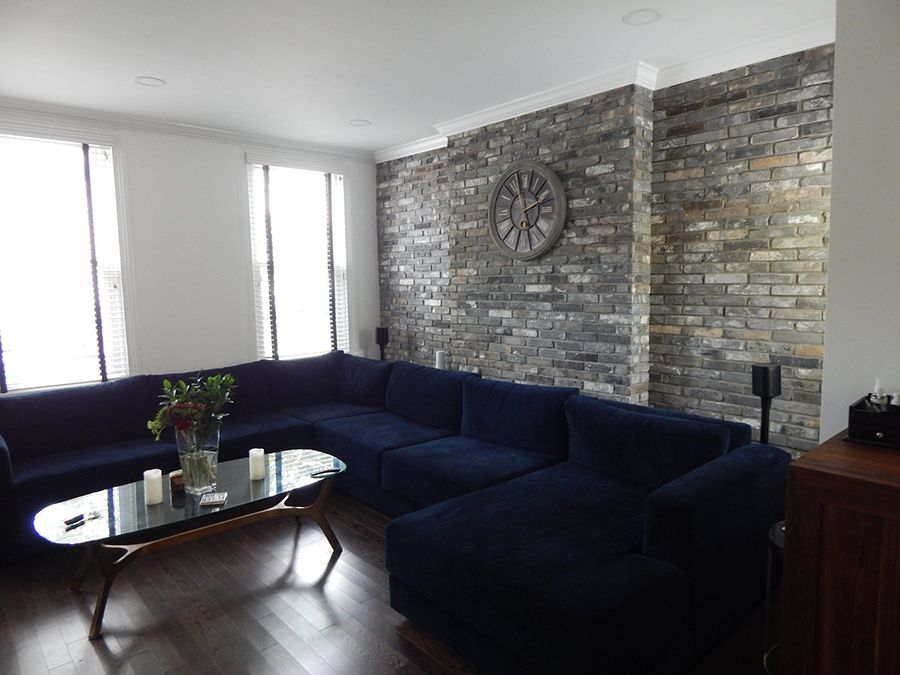 Blue sectional sofa in a living room with brick accent wall and a round clock.