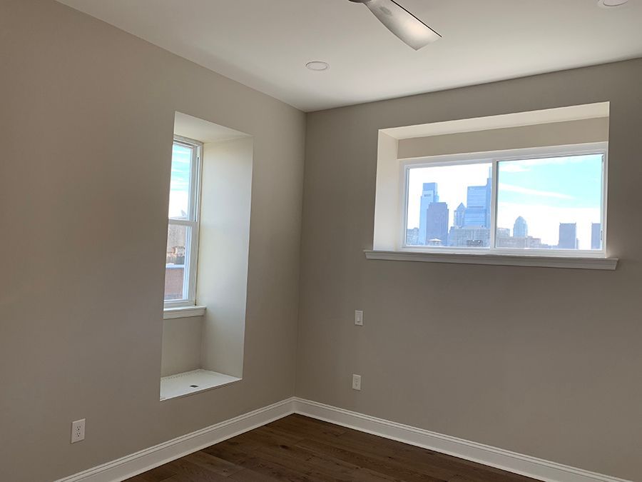 Empty room with two windows, cityscape view, light beige walls, hardwood floor.