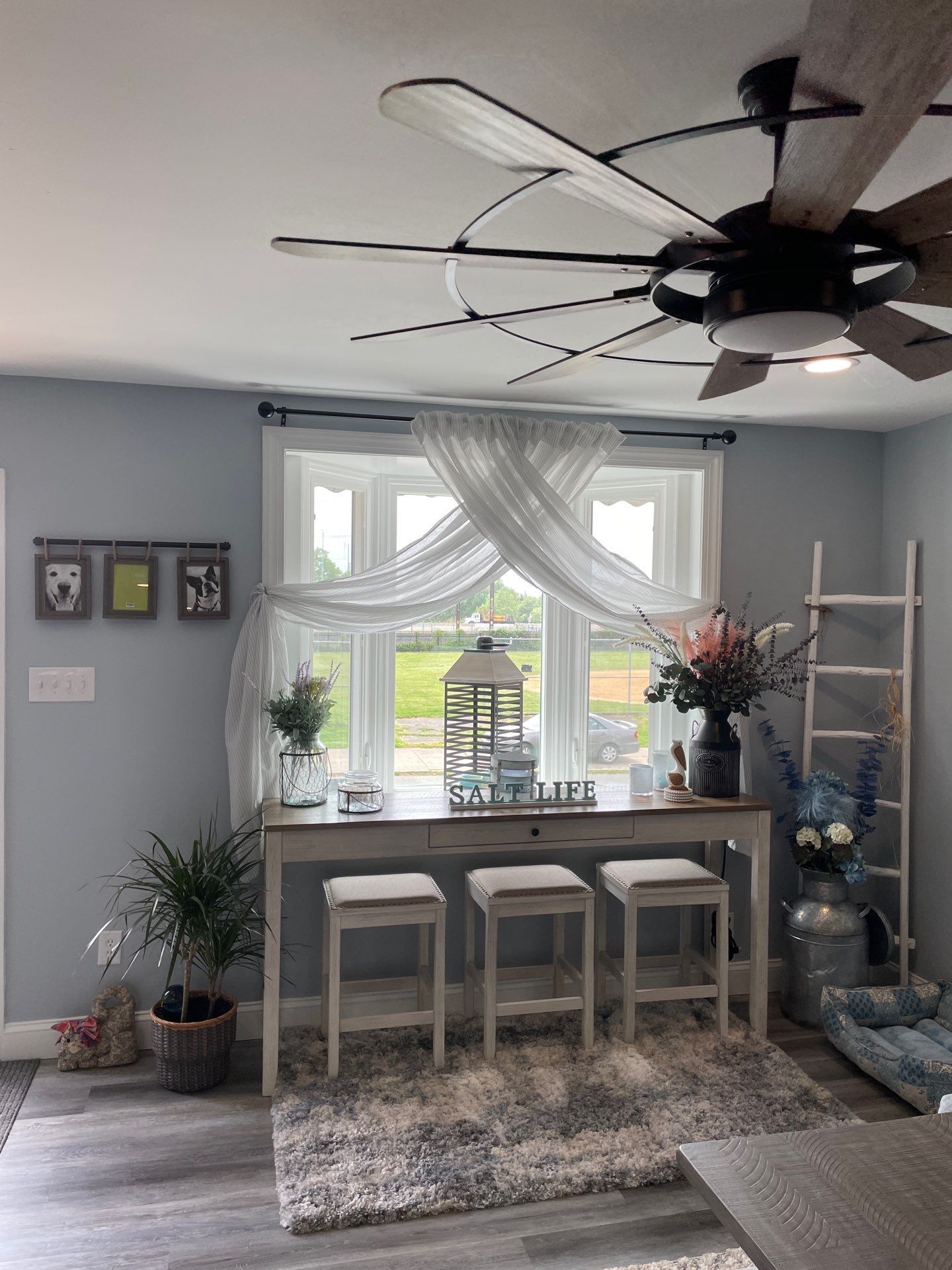 Dining area with bar table, stools, window, and decorative items. Gray walls and flooring, white and silver accents.
