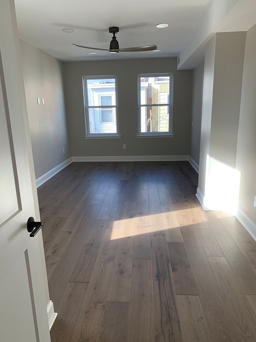 Empty room with hardwood floors, two windows, and a ceiling fan; natural light.