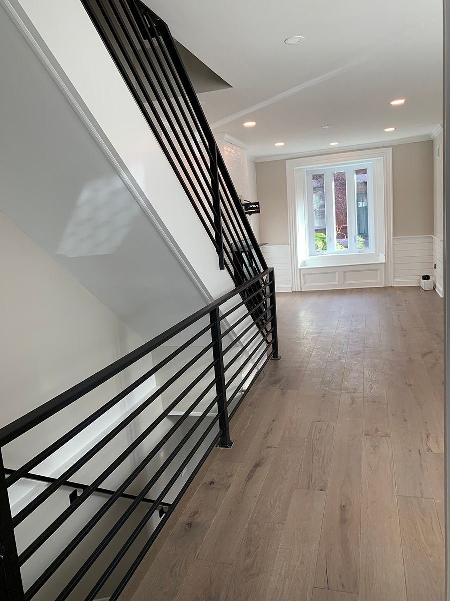 Interior view of a staircase and hallway with wood flooring. Black metal railings and white and beige walls.