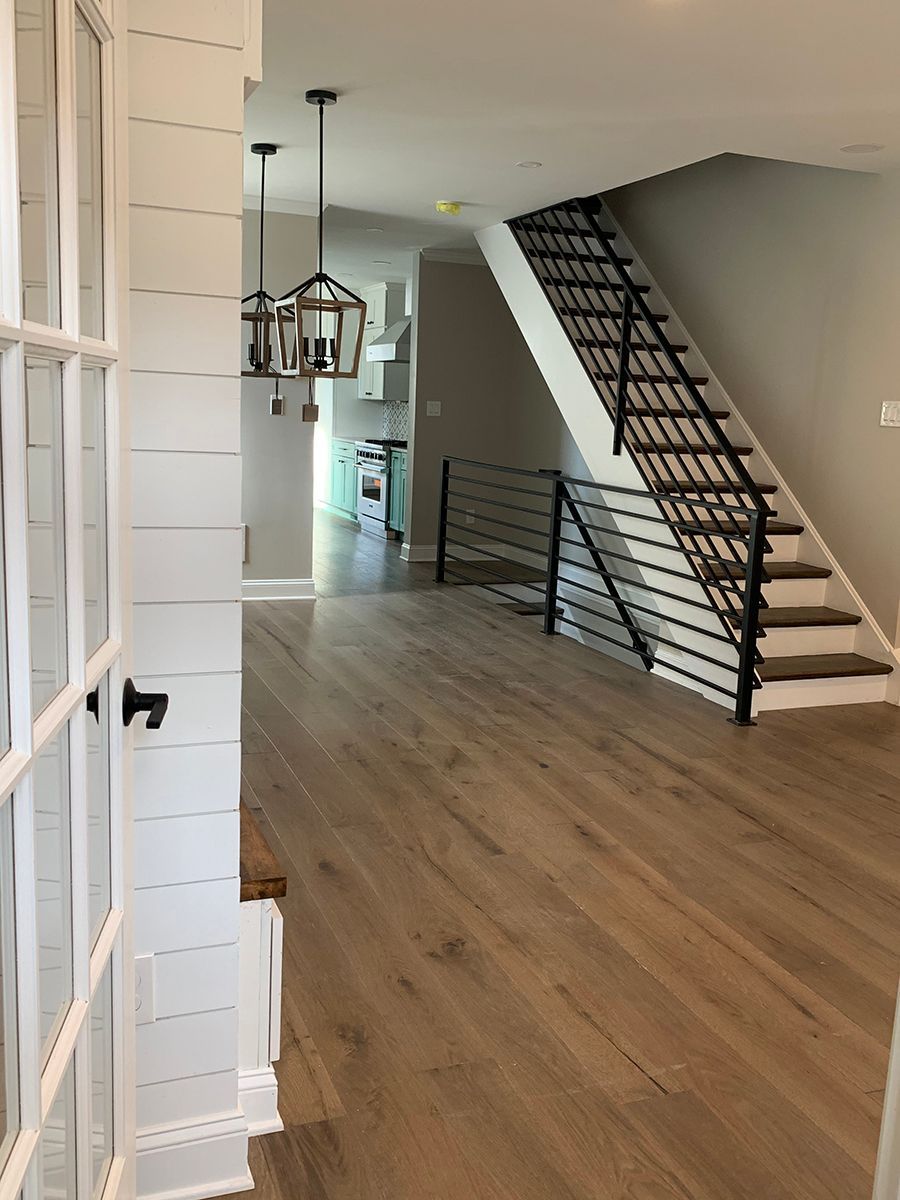Interior of a home with hardwood floors, stairs with black railing, and a view into a kitchen.