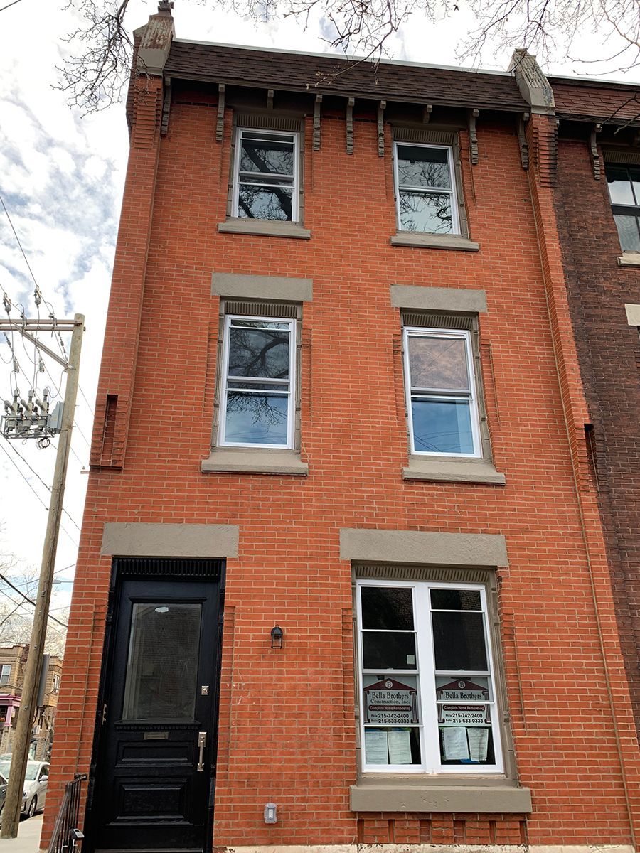 Red brick row house with black door and white-framed windows, against a cloudy sky.