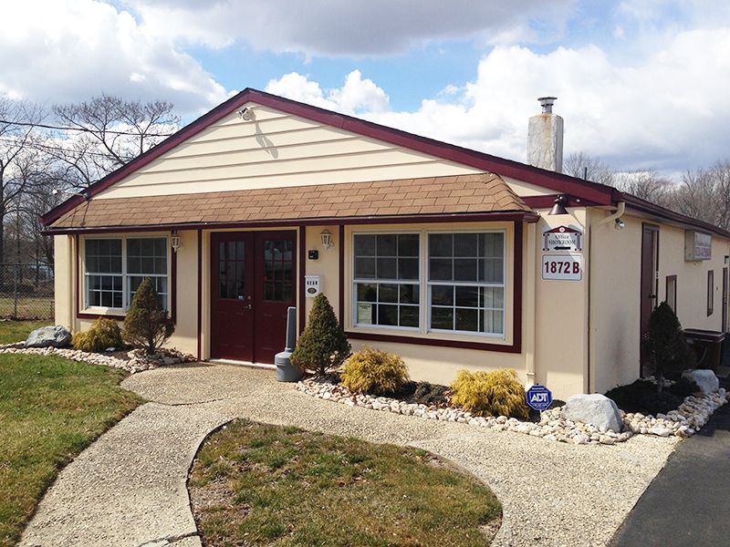 Tan building with red trim, double doors, and white-framed windows; walkway in front.