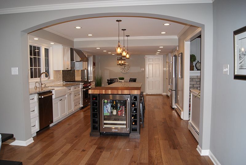 Open-concept kitchen with island and wine fridge, hardwood floors, gray walls, and archway.