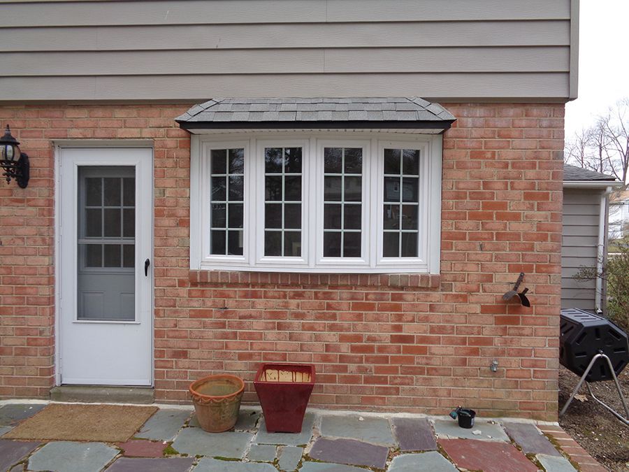 Exterior of a brick building with a white door, a bay window, and a slate patio.