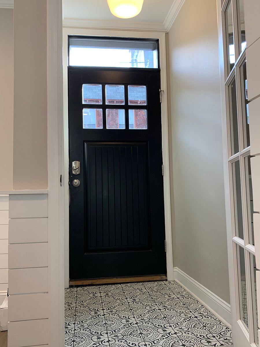 Black door with glass panes, leading to a small tiled entryway, lit by a ceiling light.