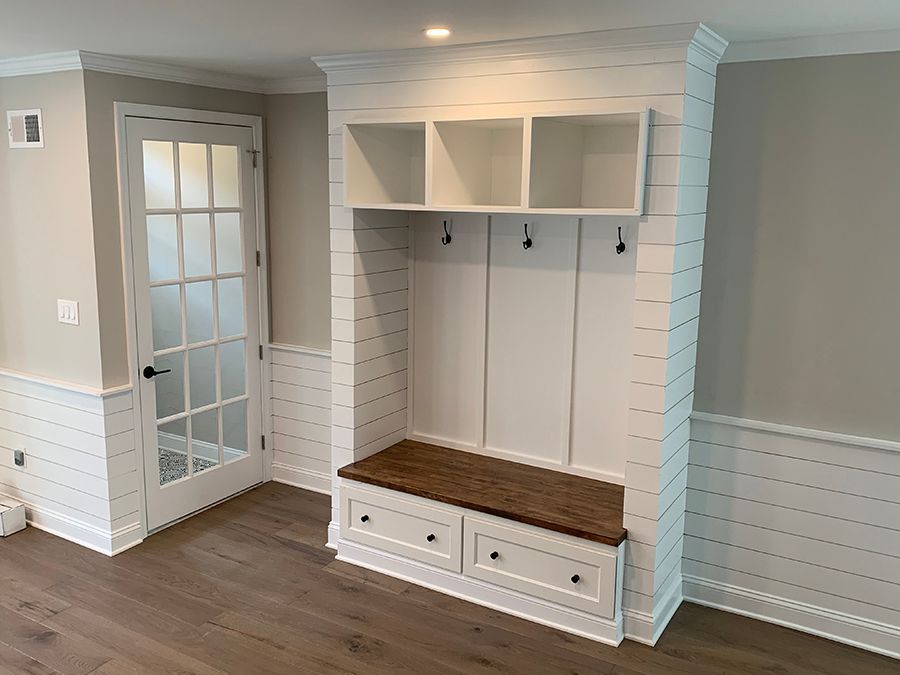 White built-in mudroom with a bench, storage, and hooks. The door is visible to the left.