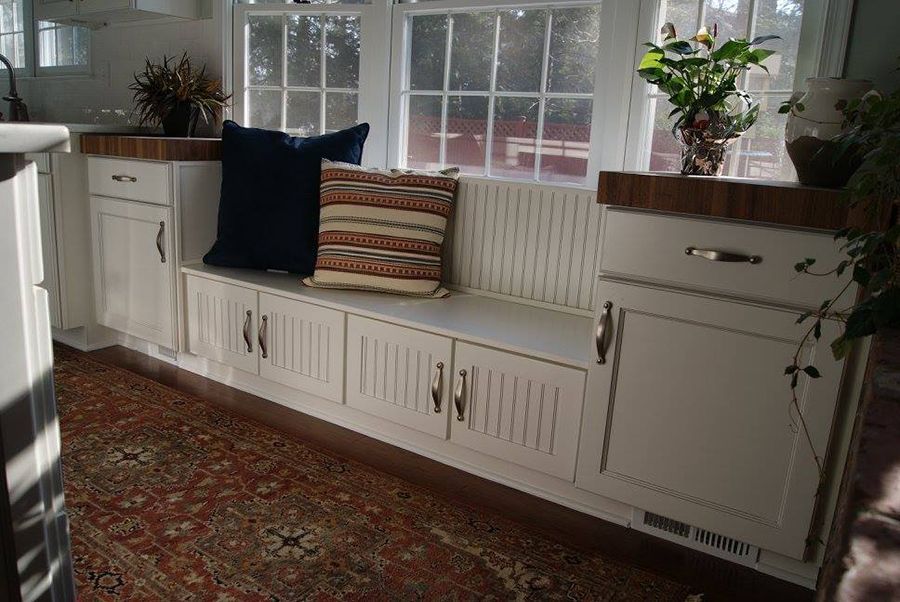 A built-in white window seat with cushions, flanked by cabinets, set against a window with sunlight.