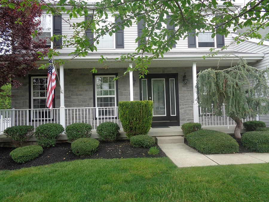 Two-story house with a front porch, bushes, and an American flag.