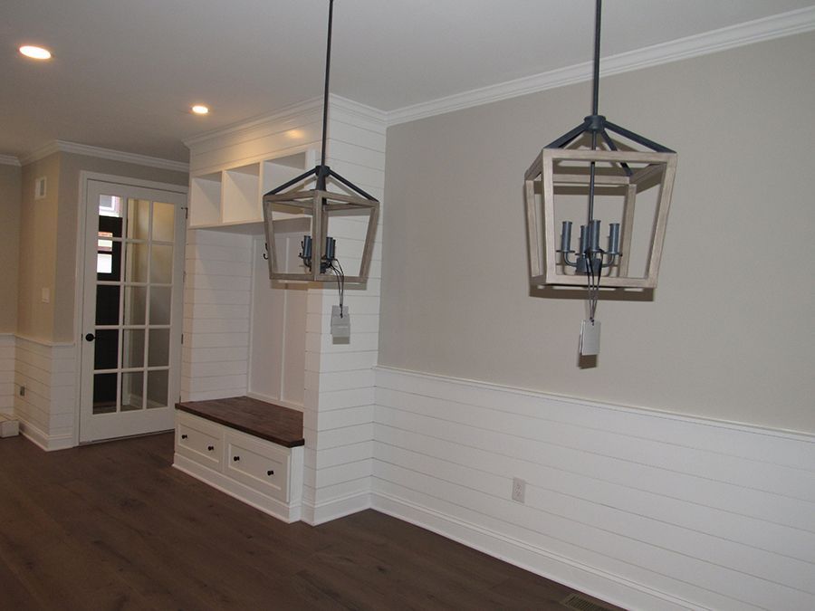 Dining room with two hanging lanterns, built-in bench, white wainscoting, and dark wood floors.