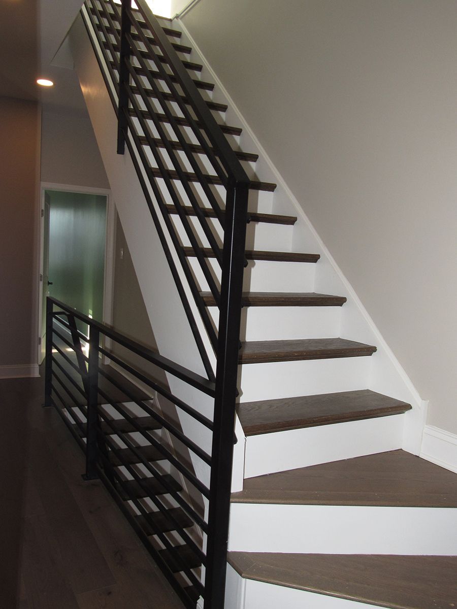 Staircase with black metal railing and white risers, brown treads, and a frosted glass door in the background.