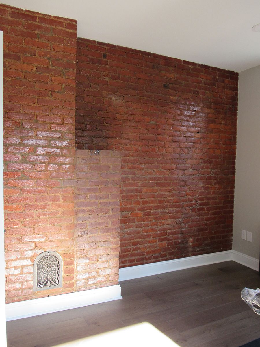 Brick wall with exposed bricks, vent, and white baseboards. Wooden floor in a room.