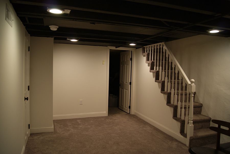 Finished basement with staircase, doorway, black ceiling, white walls, and carpeted floor.