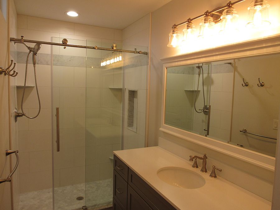 Bathroom with glass shower, white vanity, and overhead light.