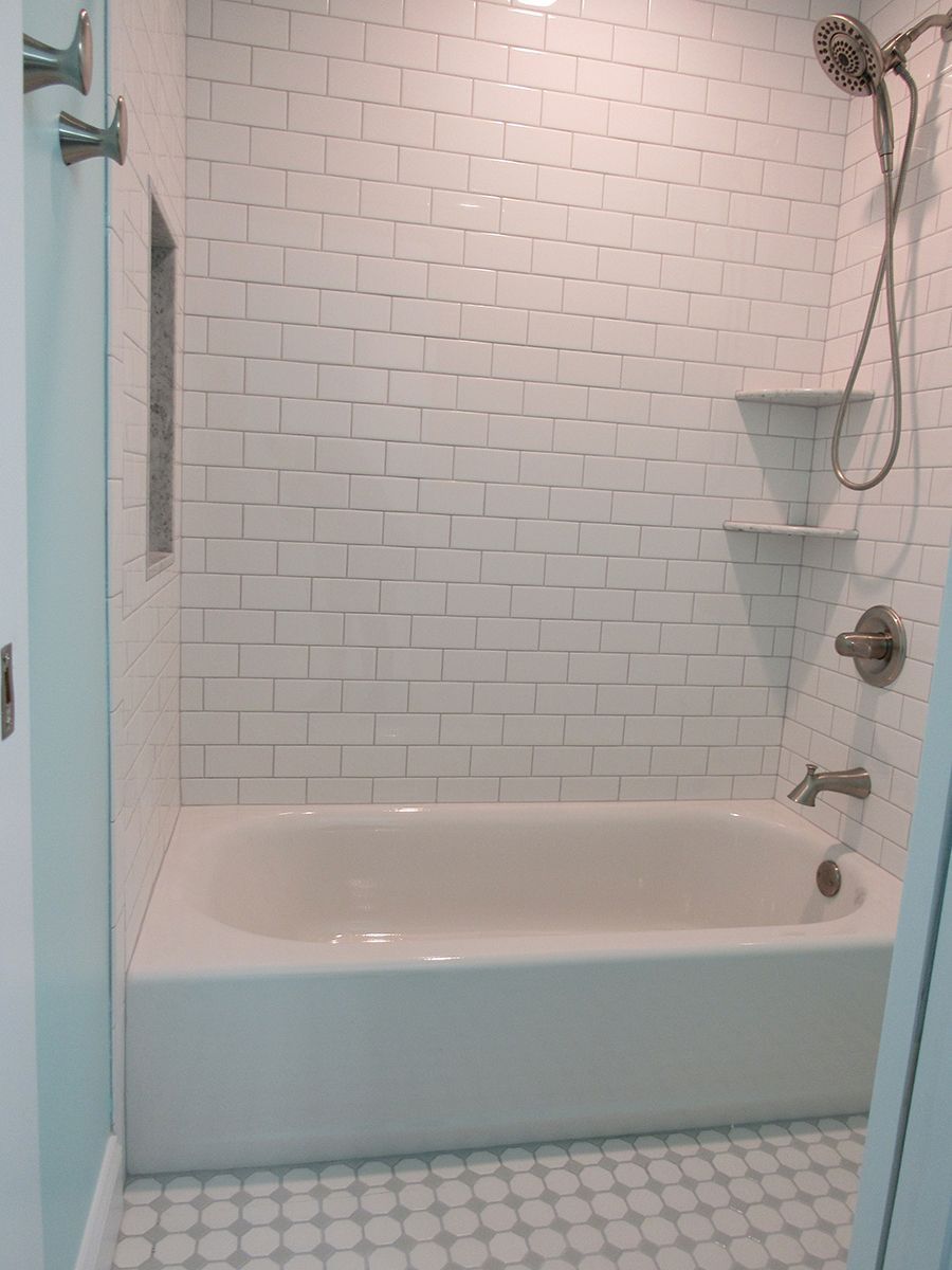 White-tiled bathroom with a bathtub, showerhead, shelves, and gray and white patterned floor tiles.