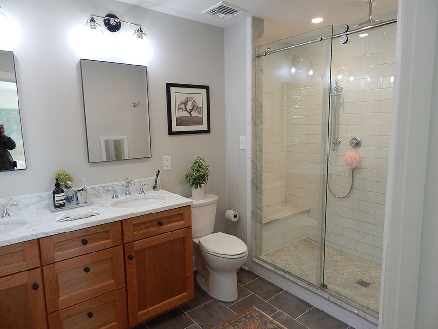 Bathroom with a vanity, toilet, and glass shower. Brown wood cabinets, white countertop. Gray walls.