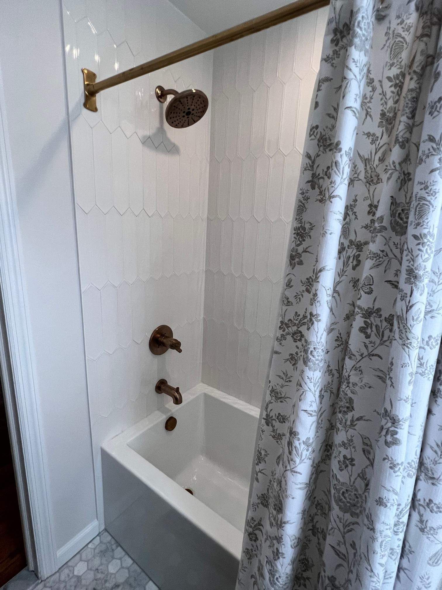 Small white tiled shower with bronze fixtures and floral shower curtain.