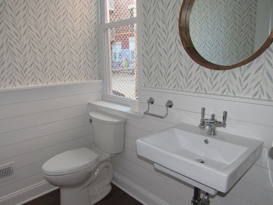 White bathroom with toilet, sink, mirror, and patterned wallpaper.